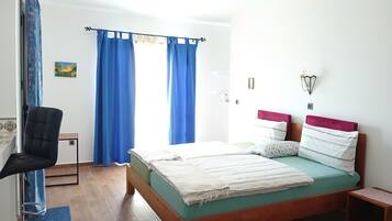 Un dormitorio con una cama, una silla, una mesita pequeña y una lámpara fijada a la pared.