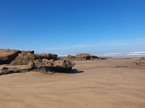 Una playa arenosa con grandes formaciones rocosas y un cielo azul despejado.