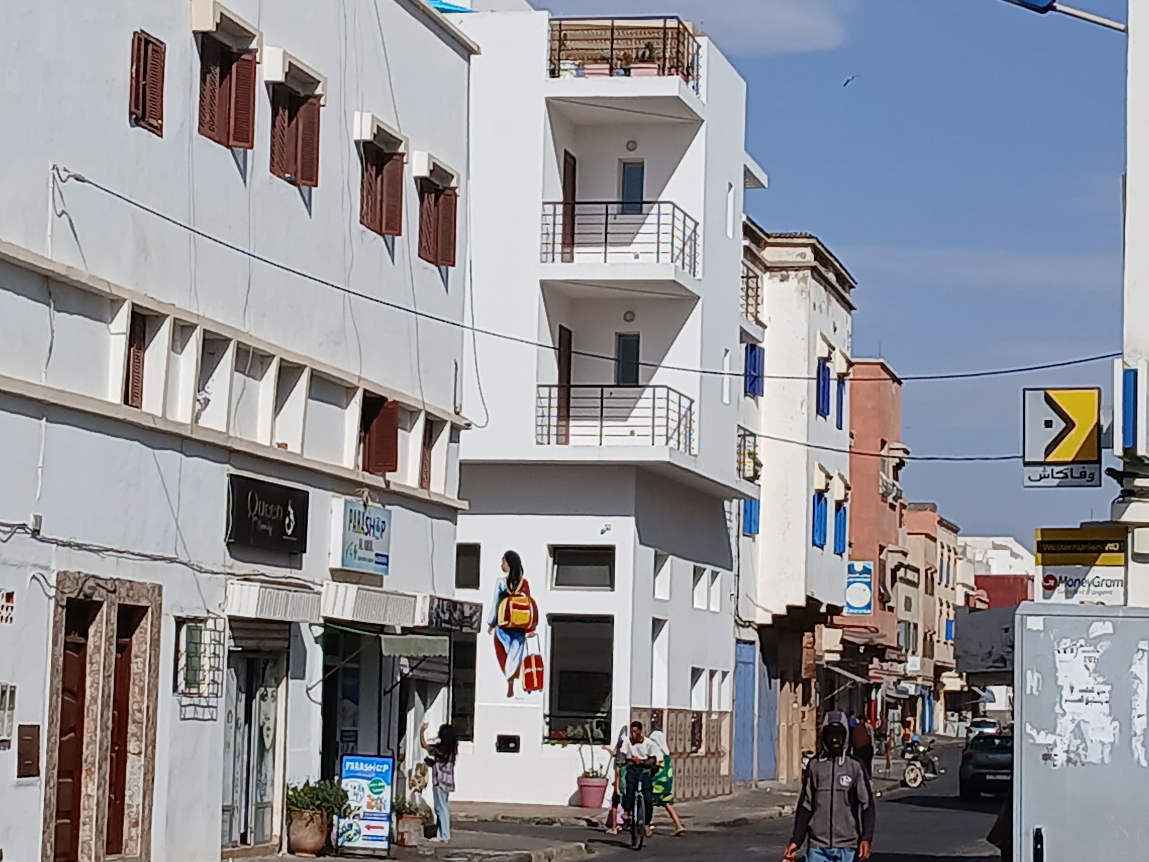 A street view with a white building featuring a balcony, a signboard, and a mural.