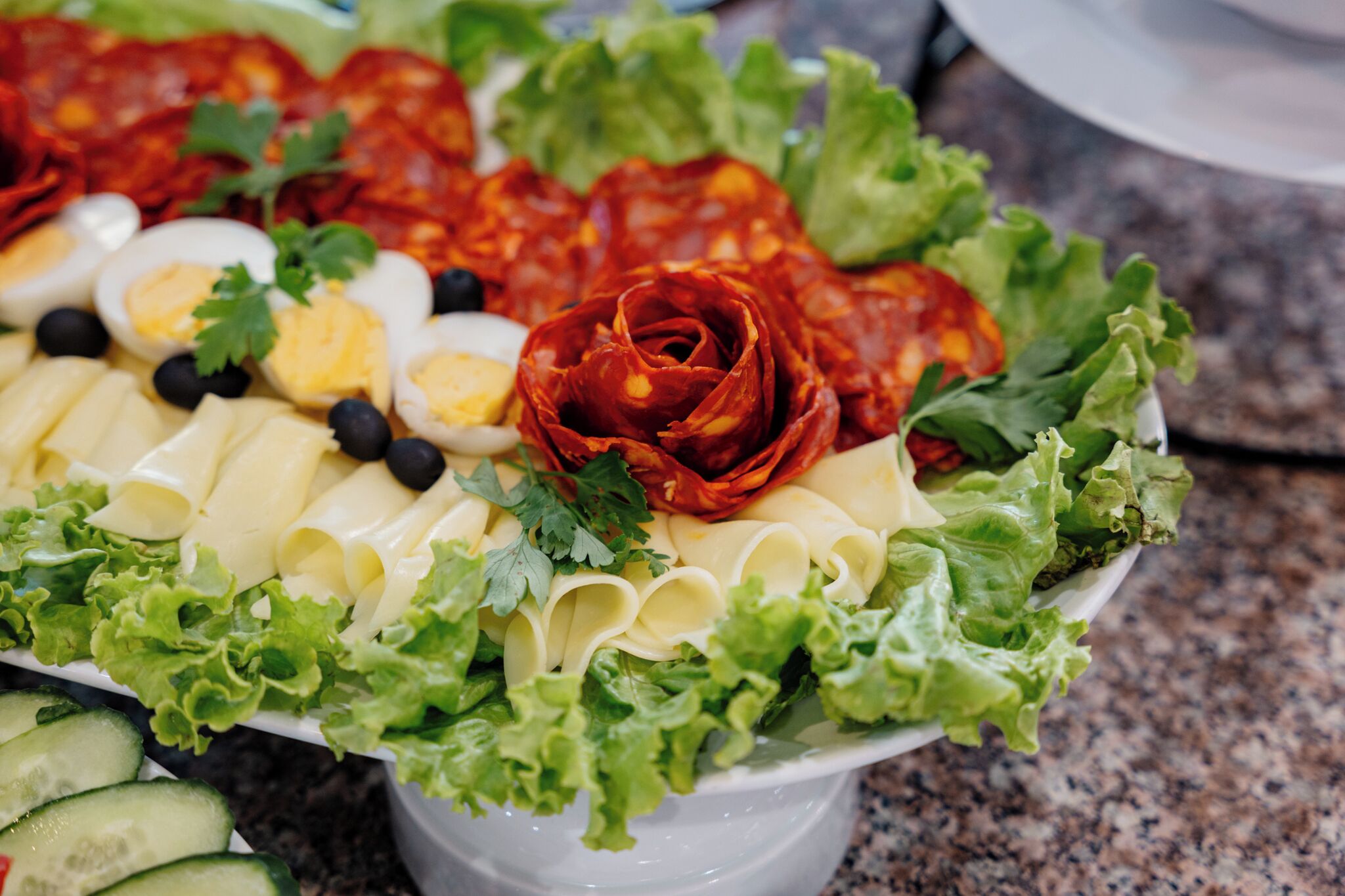 Ein Salat mit verschiedenen Zutaten, darunter Salat, Gurken, Eier, Oliven und einer dekorativen roten Blume.