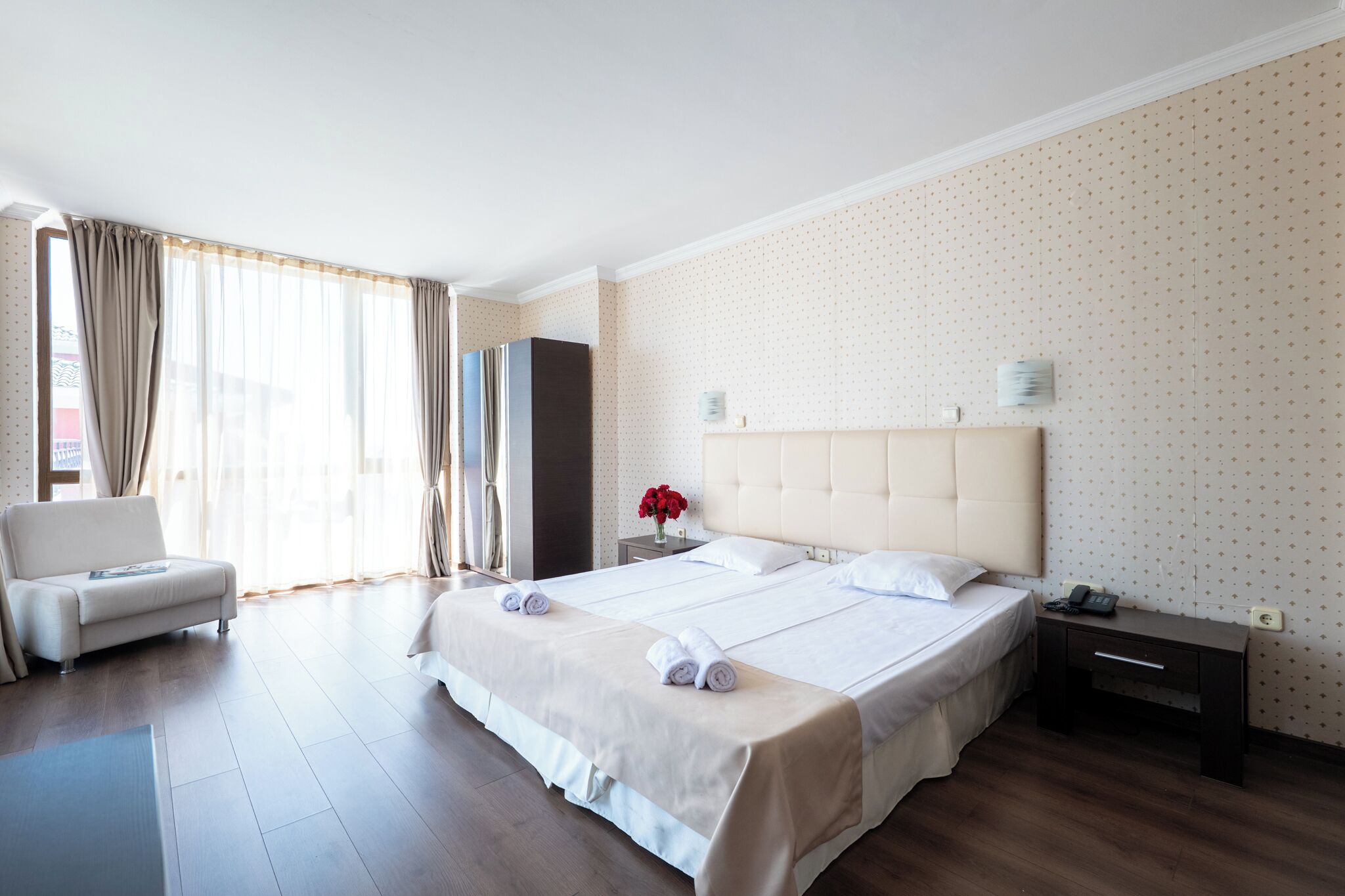 Habitación de hotel con una cama grande, una mesita de noche, una silla y una ventana con cortinas.