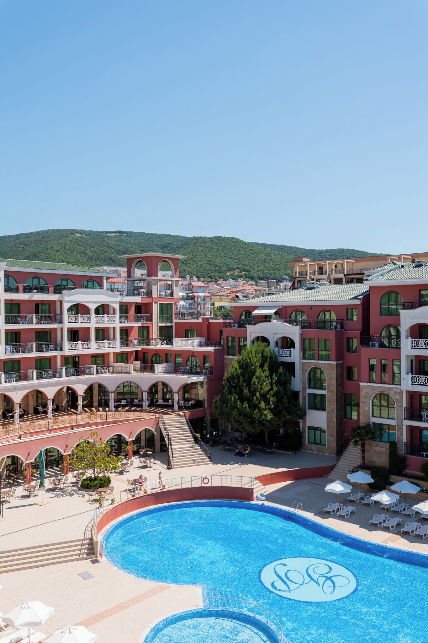 Um hotel com várias varandas, uma piscina com um logotipo e vista da região circundante.