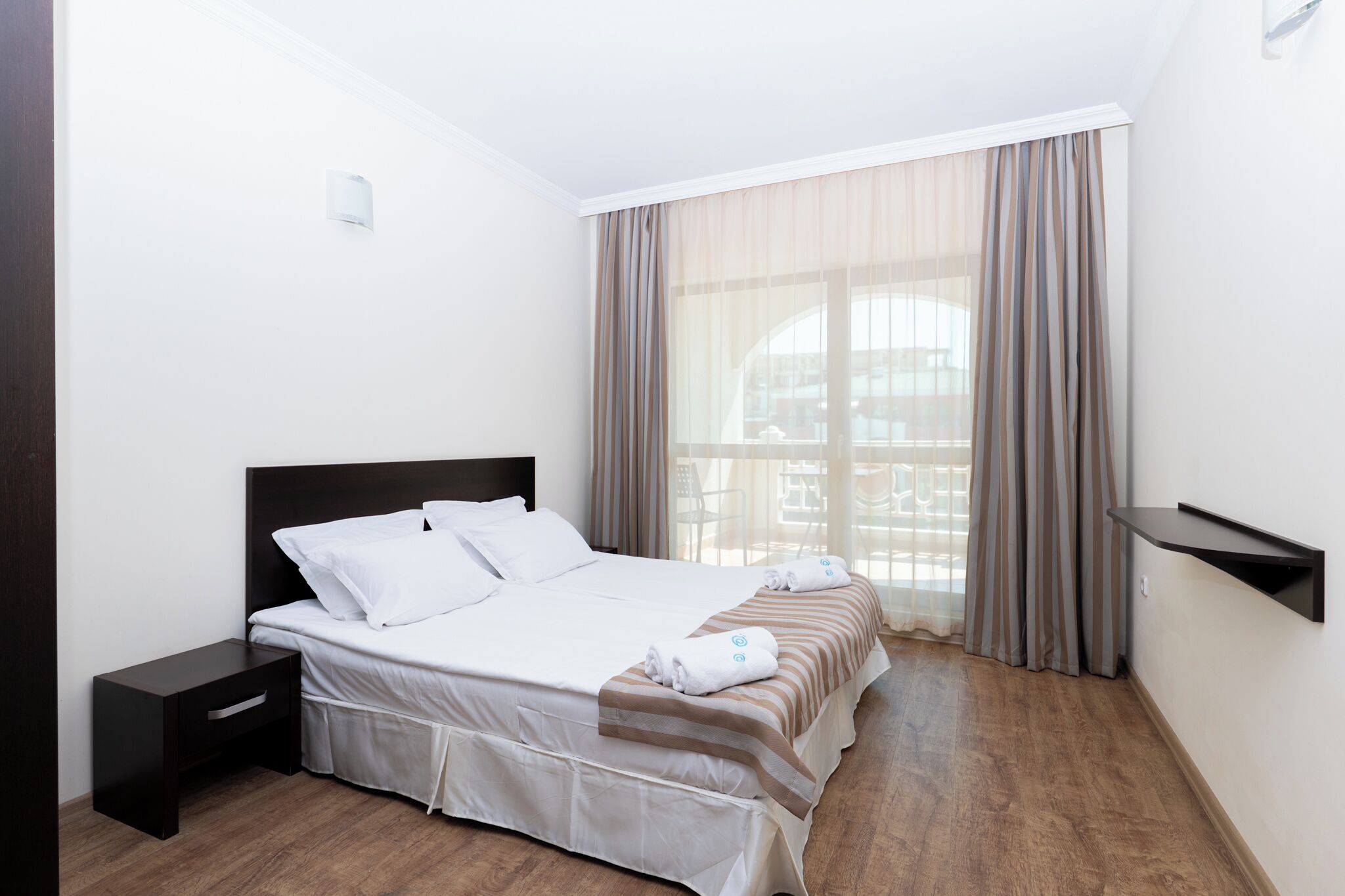 A hotel room with a bed, a nightstand, a small table, and a window with curtains.