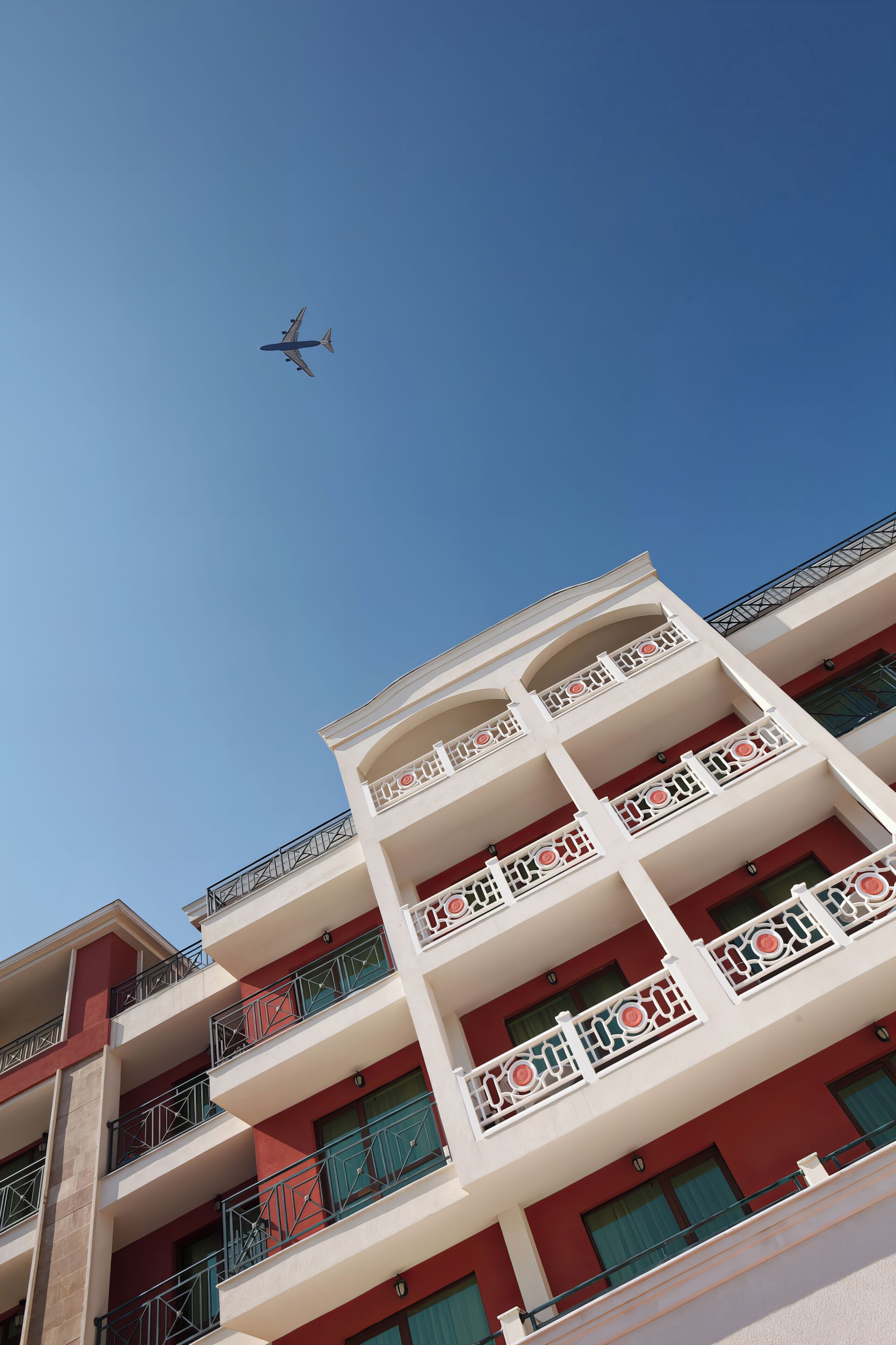A multi-story building with balconies, a clear sky, and an airplane in the distance.