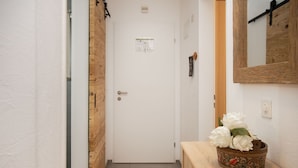 A hallway with a wooden door, a white wall, and a wooden counter with a decorative bowl of flowers. - Nice apartment for 5 people with WIFI, pool, TV, balcony and panoramic view (Falera)