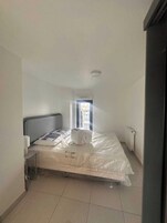 A small, clean room with a single bed, a nightstand, a window with a view, and a radiator.