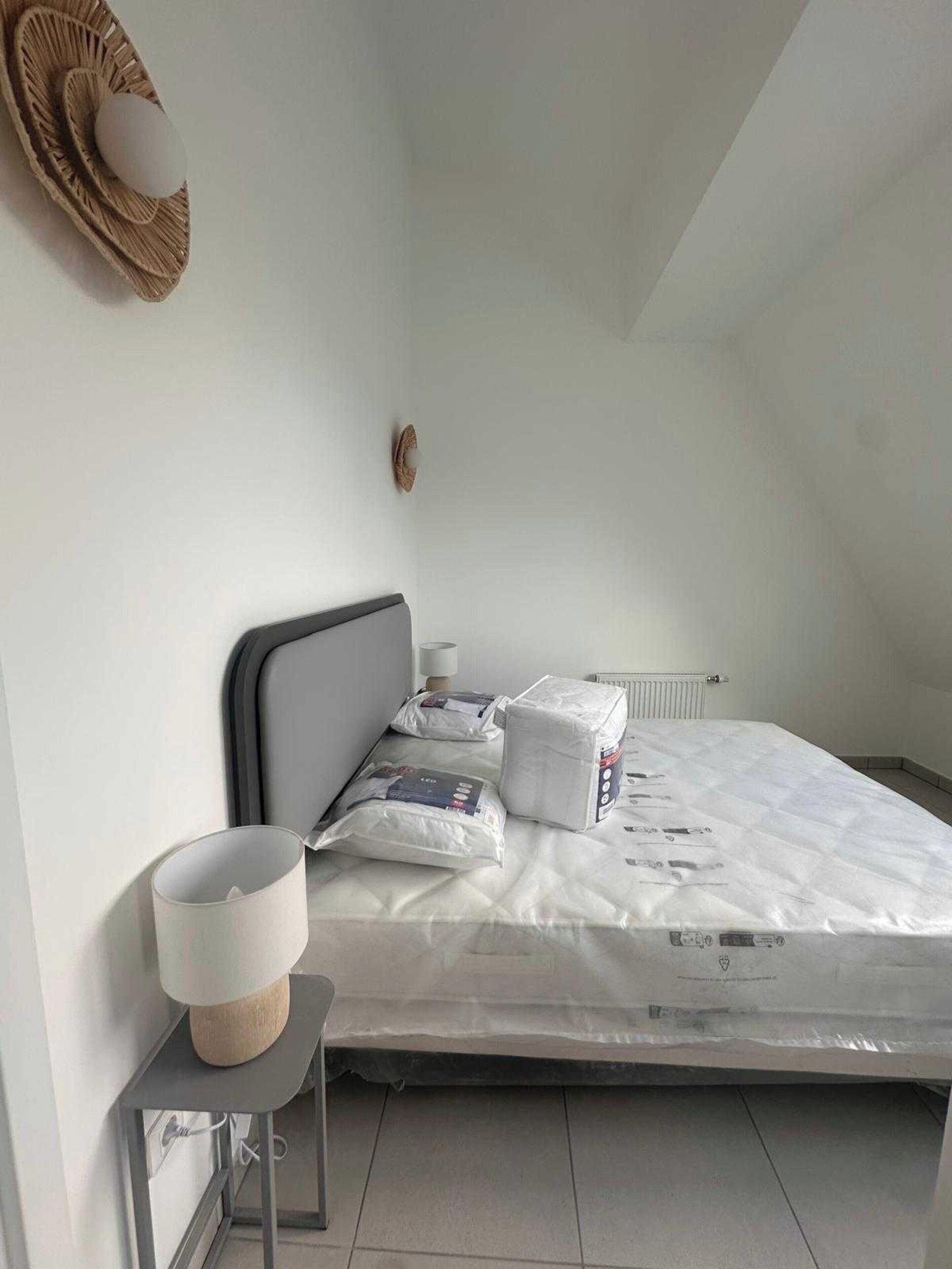 Una camera da letto con un letto, cuscini, un comodino con una lampada e un termosifone.
