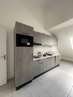 A modern kitchen with grey cabinets, a black microwave, and a marble backsplash.