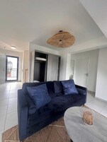 A modern living room with a dark blue sofa, a woven ceiling light fixture, and a concrete coffee table.