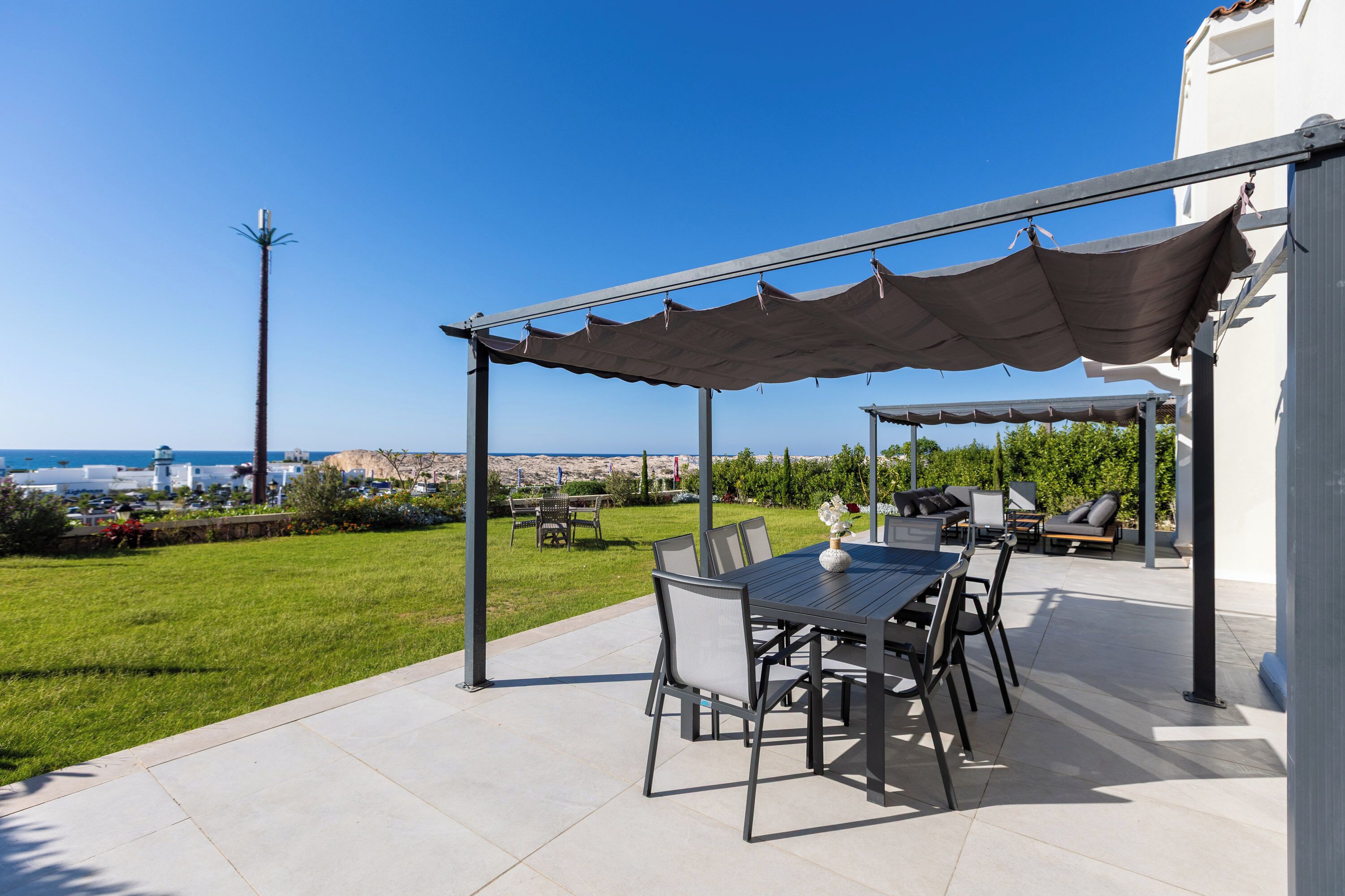 Eine Terrasse mit Tisch und Stühlen, ein überdachter Sitzbereich und Meerblick.