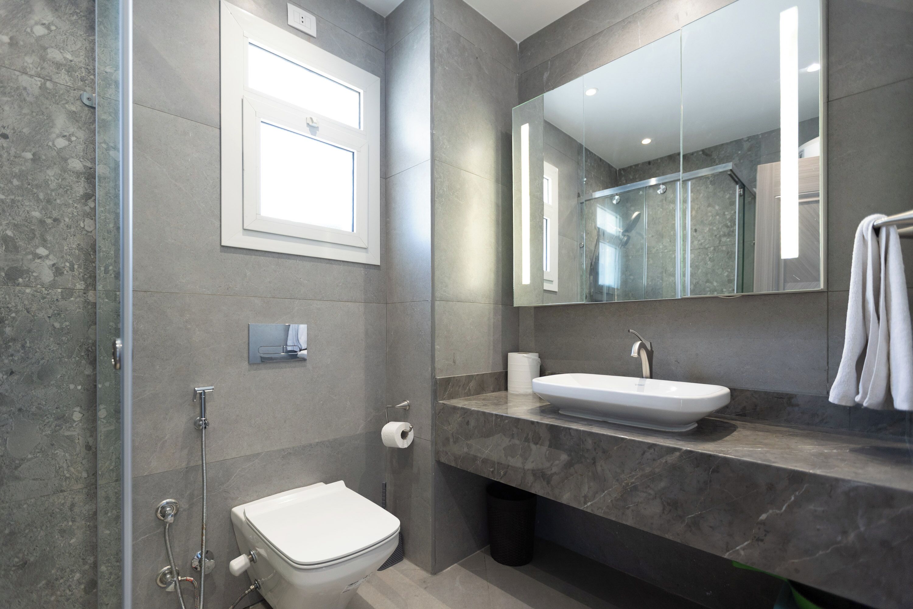 Une salle de bain moderne avec une douche à l’italienne en verre, des toilettes blanches, un comptoir en marbre et un grand miroir.