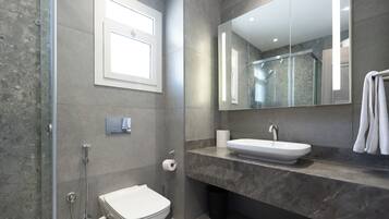 Une salle de bain moderne avec une douche à l’italienne en verre, des toilettes blanches, un comptoir en marbre et un grand miroir.