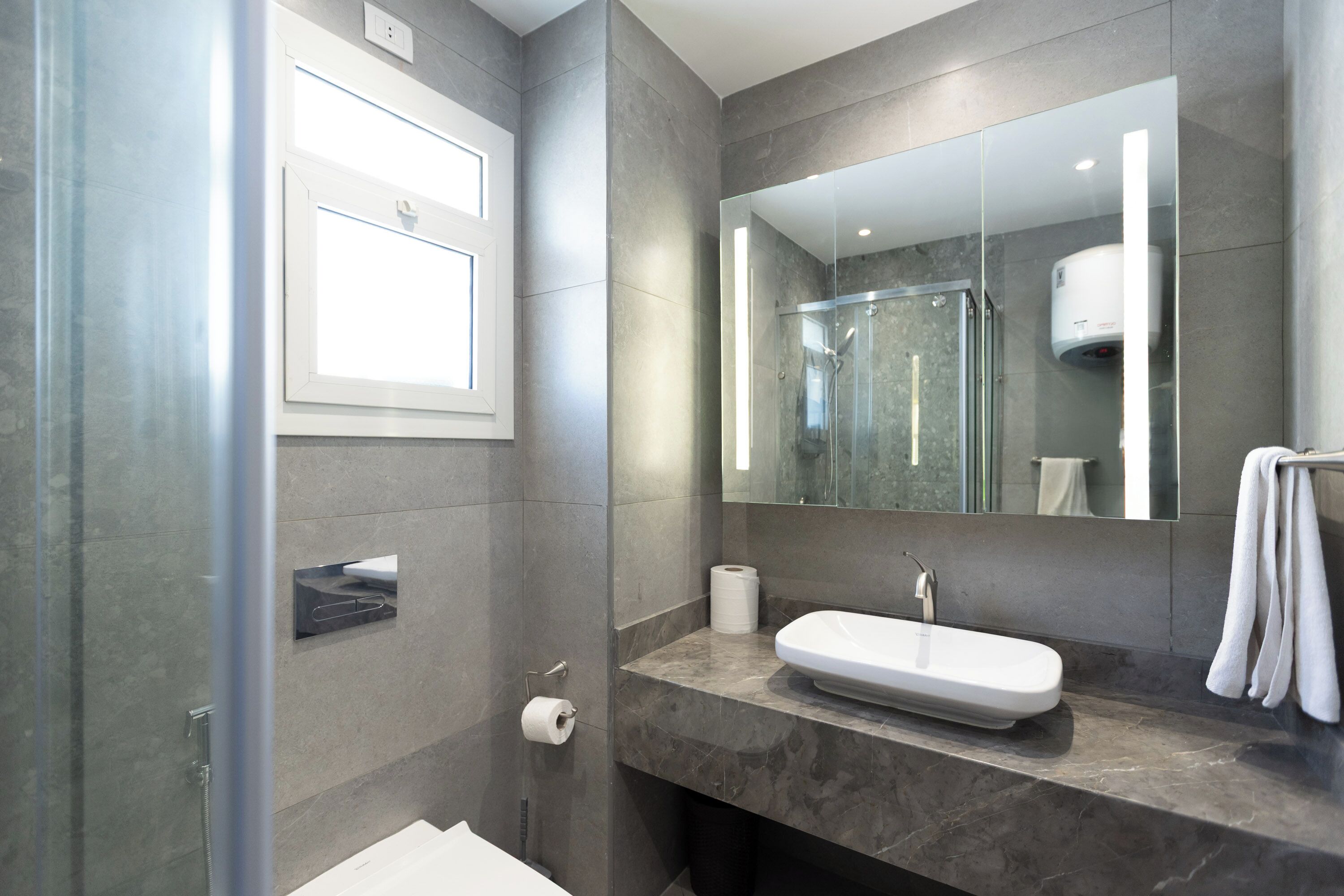 Un baño moderno con cabina de ducha de vidrio, lavabo blanco y un espejo grande.