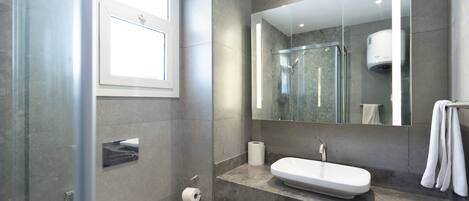 Un baño moderno con cabina de ducha de vidrio, lavabo blanco y un espejo grande.