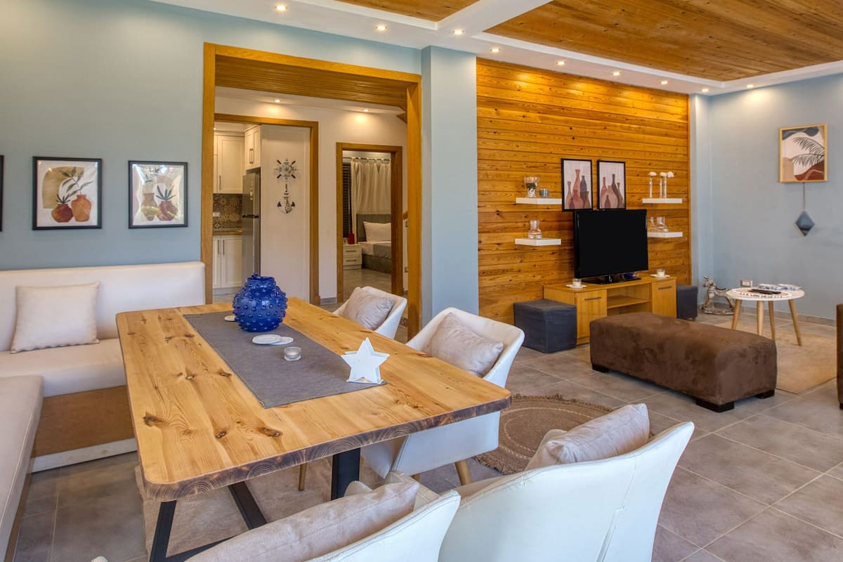 A modern living room with a wooden dining table, white sofas, and a TV.