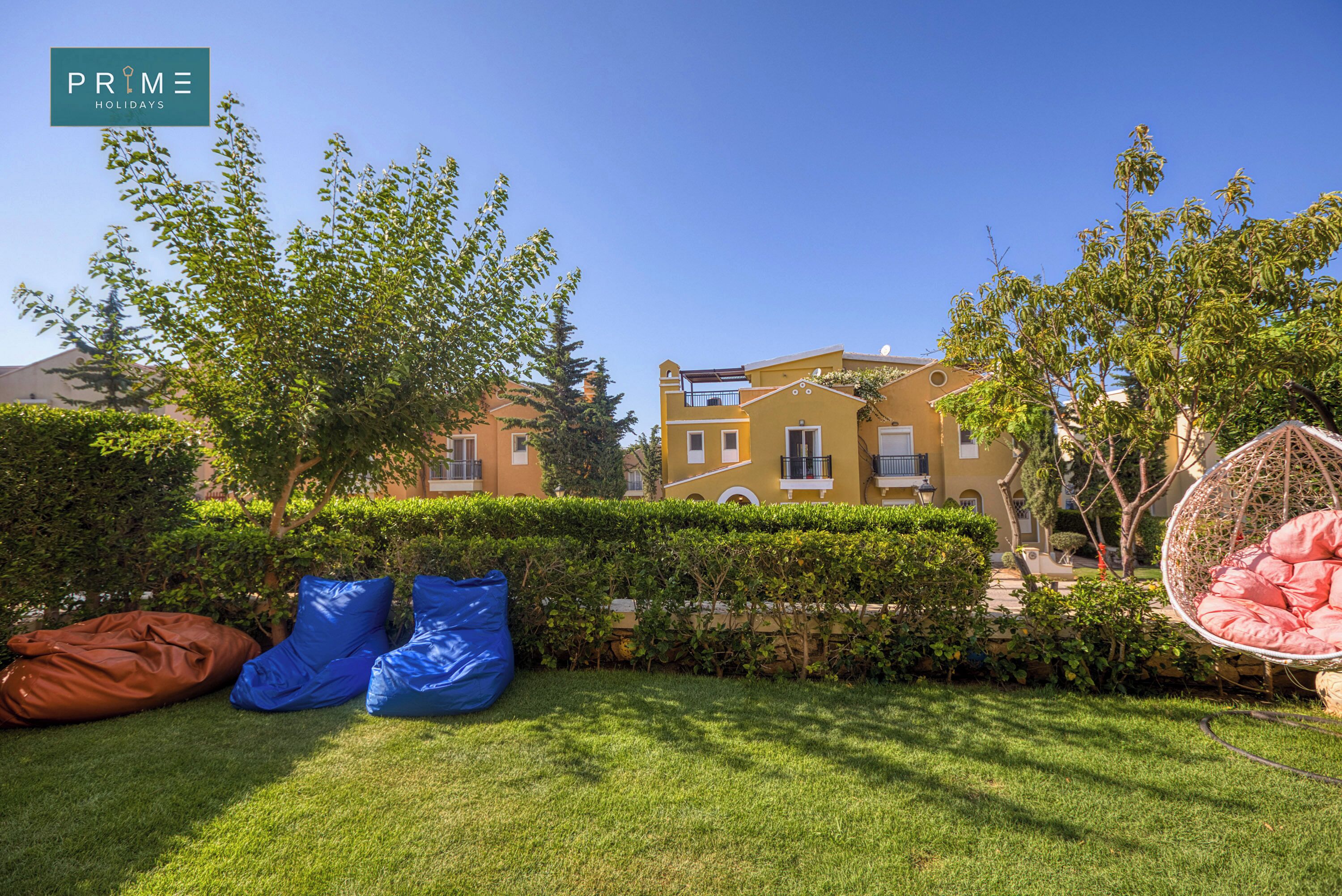 Un jardín cuidado con seto, una silla colgante y un edificio al fondo.