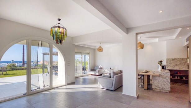 A spacious living area with a large sliding glass door leading to a balcony, a modern chandelier, and a marble countertop in the kitchen area. - Prime Holidays Mountain View Ras ElHekma (El Dabaa)