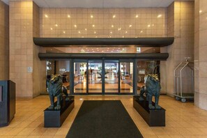 Entrada de hotel con puerta de vidrio, dos estatuas de leones, piso de baldosas y un carrito de metal.