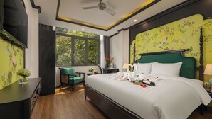 Un dormitorio con una cama grande, una silla verde, un escritorio y una ventana con vistas a árboles.