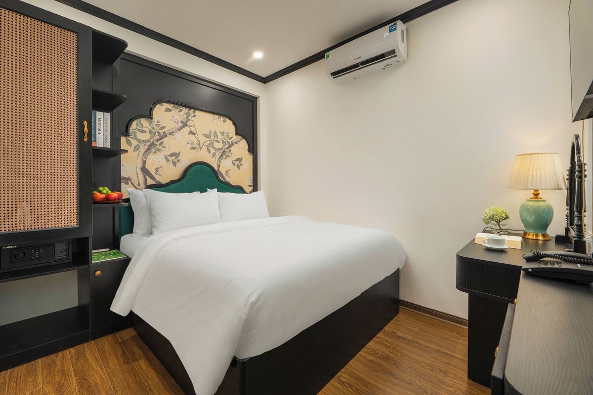 A neatly arranged hotel room with a bed, a desk, and a wall-mounted air conditioner.