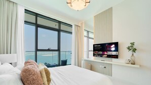 Una habitación de hotel moderna con una cama grande, un televisor montado en la pared y vistas al mar a través de ventanas amplias.