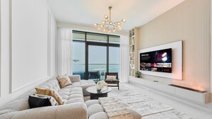 Una sala de estar moderna con un televisor de pantalla plana grande, un sofá seccional y un balcón con vista al mar.