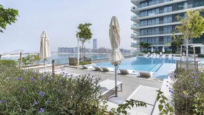 Piscina en la azotea con sillones de descanso y sombrillas, con vistas a un paisaje urbano y una masa de agua.