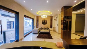 A modern hotel room with a large bed, a sitting area with a sofa and armchairs, a marble floor, and a view of the street through large windows. - THE MAJESTIC GRAND (Chandigarh)