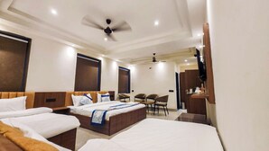 A hotel room with two beds, a desk, a chair, a TV, and a ceiling fan. - THE MAJESTIC GRAND (Chandigarh)