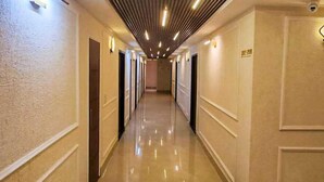A long, well-lit hallway with a modern ceiling design, leading to multiple doors on both sides. - THE MAJESTIC GRAND (Chandigarh)