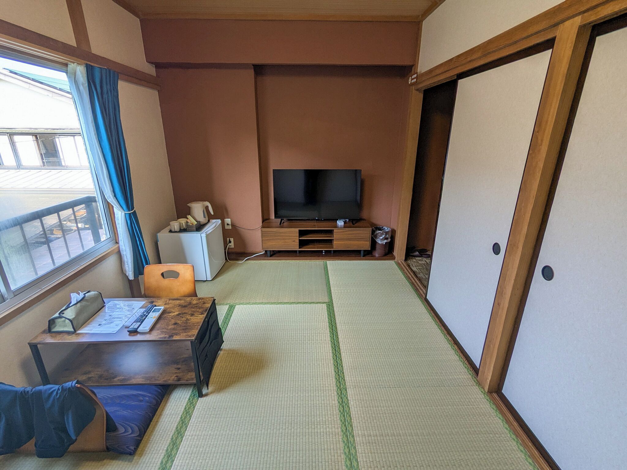 A room with tatami mats, a television, a small refrigerator, and a wooden cabinet.