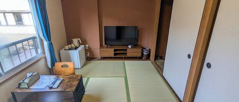A room with tatami mats, a television, a small refrigerator, and a wooden cabinet.