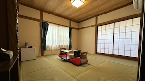 Una habitación japonesa tradicional con suelo de tatami, una mesa baja con cojines, una cama futón y una ventana con pantalla shoji.