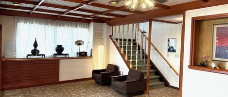 A room with a wooden ceiling, a staircase, a sofa, and a desk with decorative items.