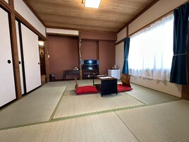 A traditional Japanese-style room with tatami flooring, a low table with cushions, a television, and sliding doors.