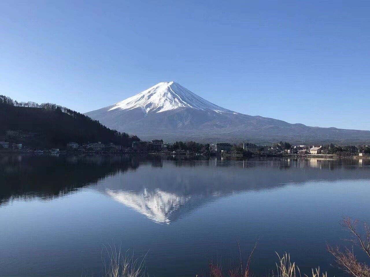 A calm lake reflecting a snow-capped mountain, with a town in the foreground.
