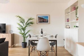 A modern dining area with a table set for two, a potted plant, and a television on a stand. - Dify Bollier - Quartier Gerland (Lyon)