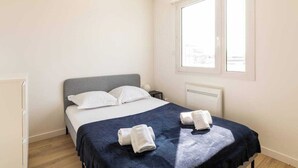 A bedroom with a bed, white pillows, a dark blue bedspread, and two towels on the bed. - Dify Bollier - Quartier Gerland (Lyon)