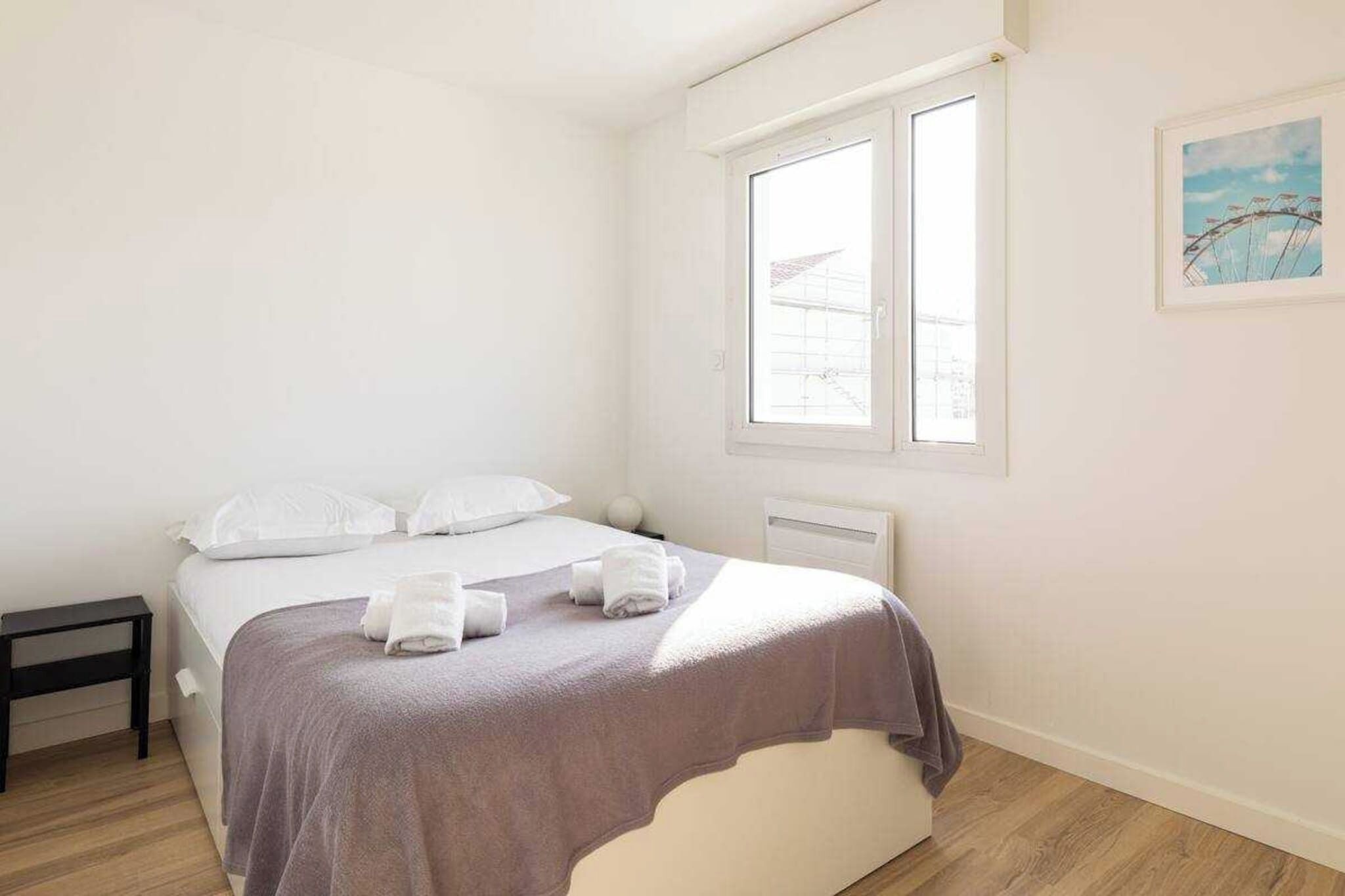 Une chambre à coucher avec un lit, une table de chevet, une fenêtre et un tableau accroché au mur.
