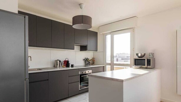 A modern kitchen with dark cabinets, a central island, and a large window providing natural light. - Dify Bollier - Quartier Gerland (Lyon)