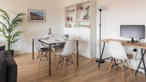 A modern dining area with a wooden table, white chairs, and a bookshelf. - Dify Bollier - Quartier Gerland (Lyon)