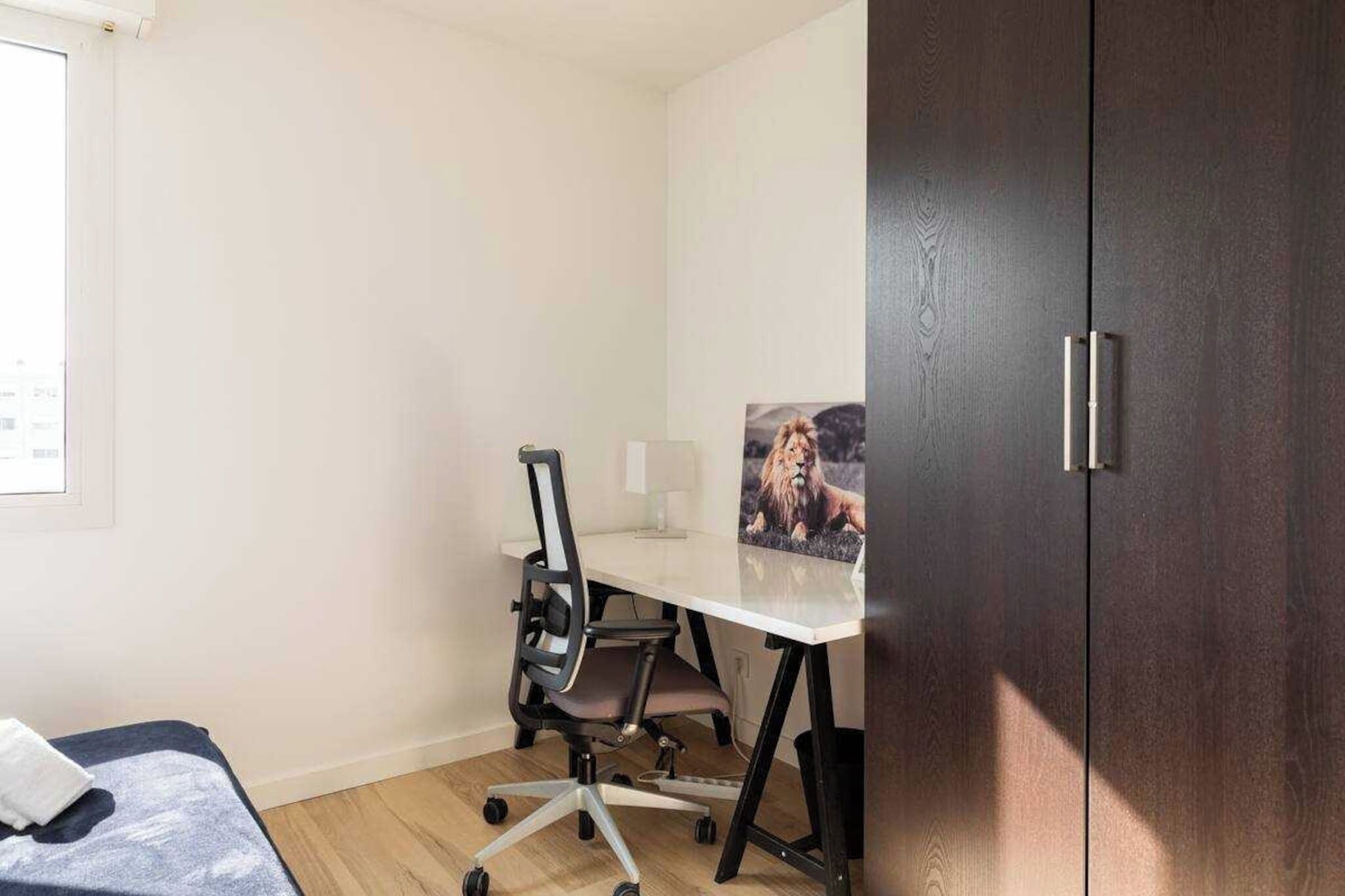 Een kleine, goed verlichte kamer met een bureau, stoel en een lijst met een foto aan de muur.