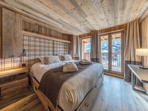 A wooden-paneled bedroom with a bed, a nightstand, a window with a view, and a table with a lamp.