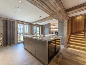 A modern kitchen with a large island, wooden beams, and a view of a residential building.