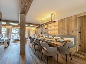 A dining area with a long wooden table, grey upholstered chairs, and a wooden wall with built-in lighting. - Luxurious 6-room apartment with hammam, fireplace and parking in Val-d'Isère (Val-d'Isère)
