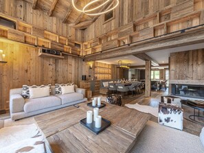 Amplia sala de estar con techo de madera, un conjunto de sofás, una mesa de centro con velas y una chimenea.