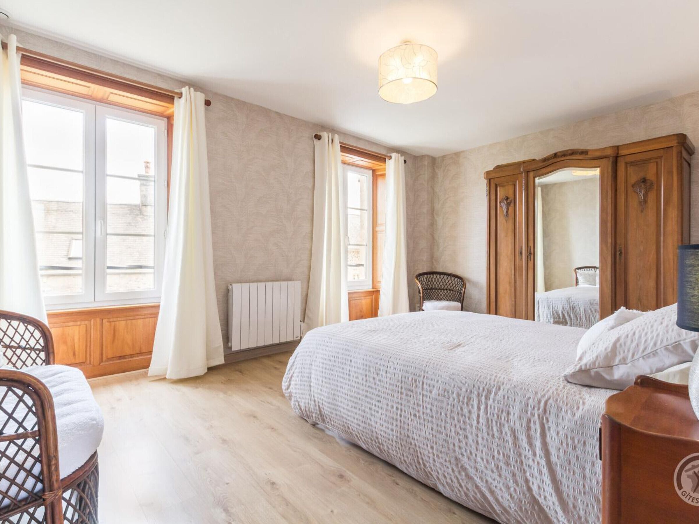 A bedroom with a large bed, wooden wardrobe, and a chair.