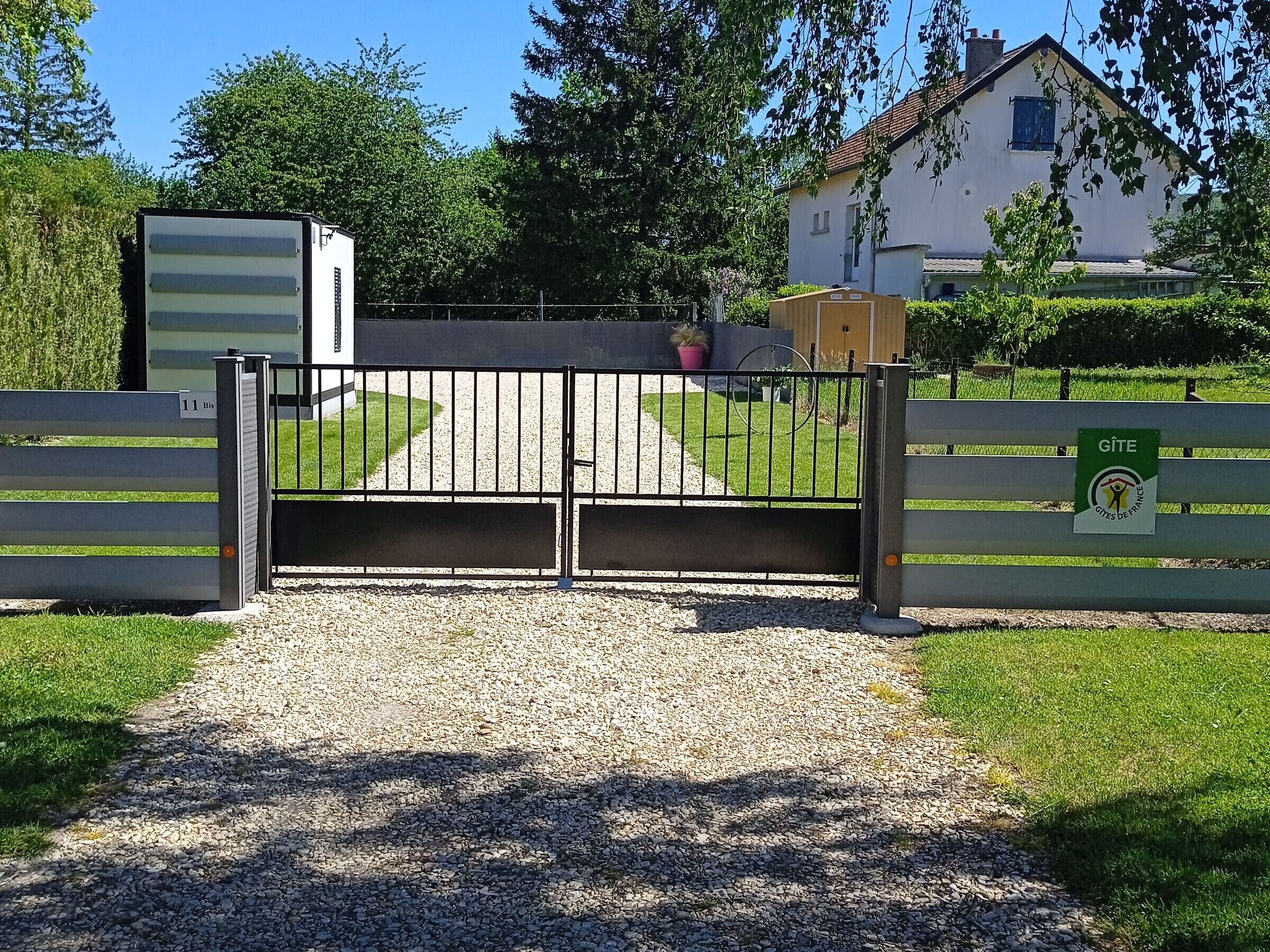 Une entrée fermée par un portail, avec un chemin de gravier menant à un bâtiment.