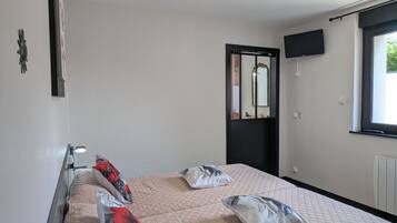 Ein Hotelzimmer mit Bett, einem an der Wand montierten Fernseher und einem Fenster mit Blick auf Grünflächen.