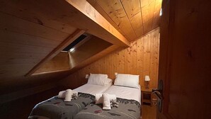 A cozy attic bedroom with a sloped ceiling, wooden walls, a double bed with two pillows, a bedside lamp, and a small table. - 9-person apartment with parking in Tignes Val Claret (Tignes)